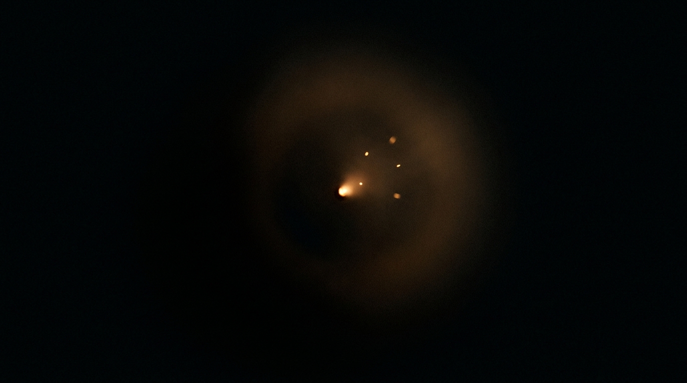 Ein einzelner warmer Lichtfunke glimmt in völliger Dunkelheit, einige Funken lösen sich.