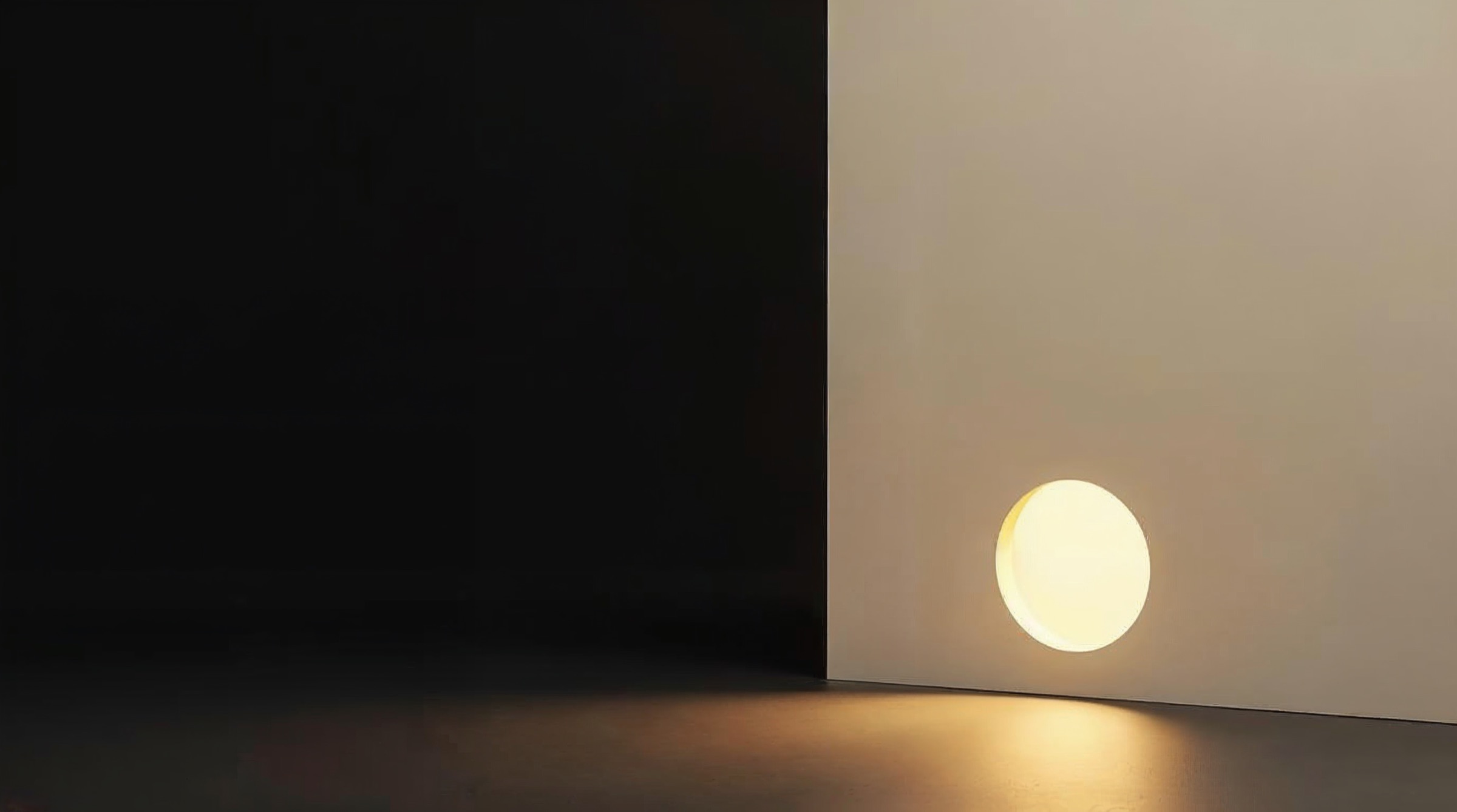 Eine warme Lichtscheibe leuchtet aus einer runden Öffnung in einer hellen Wand, davor dunkler Boden.