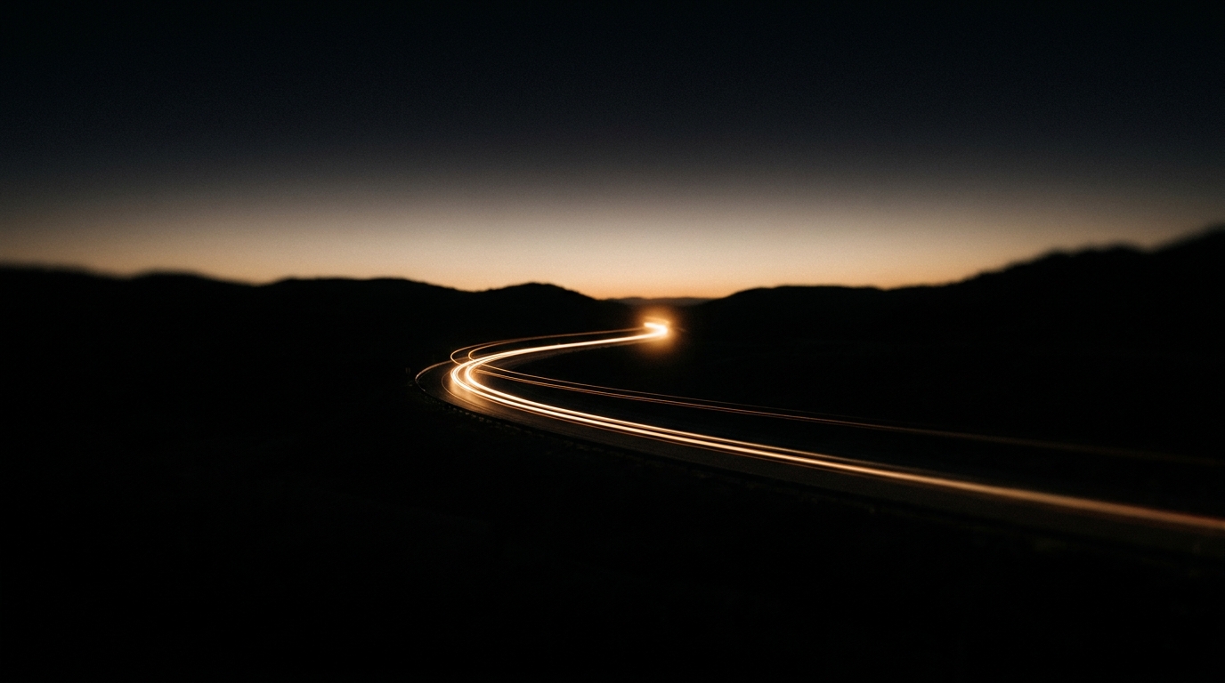 Ein einzelnes Auto auf leerer Landstraße im Morgengrauen, goldene Lichtspuren in der Langzeitbelichtung.